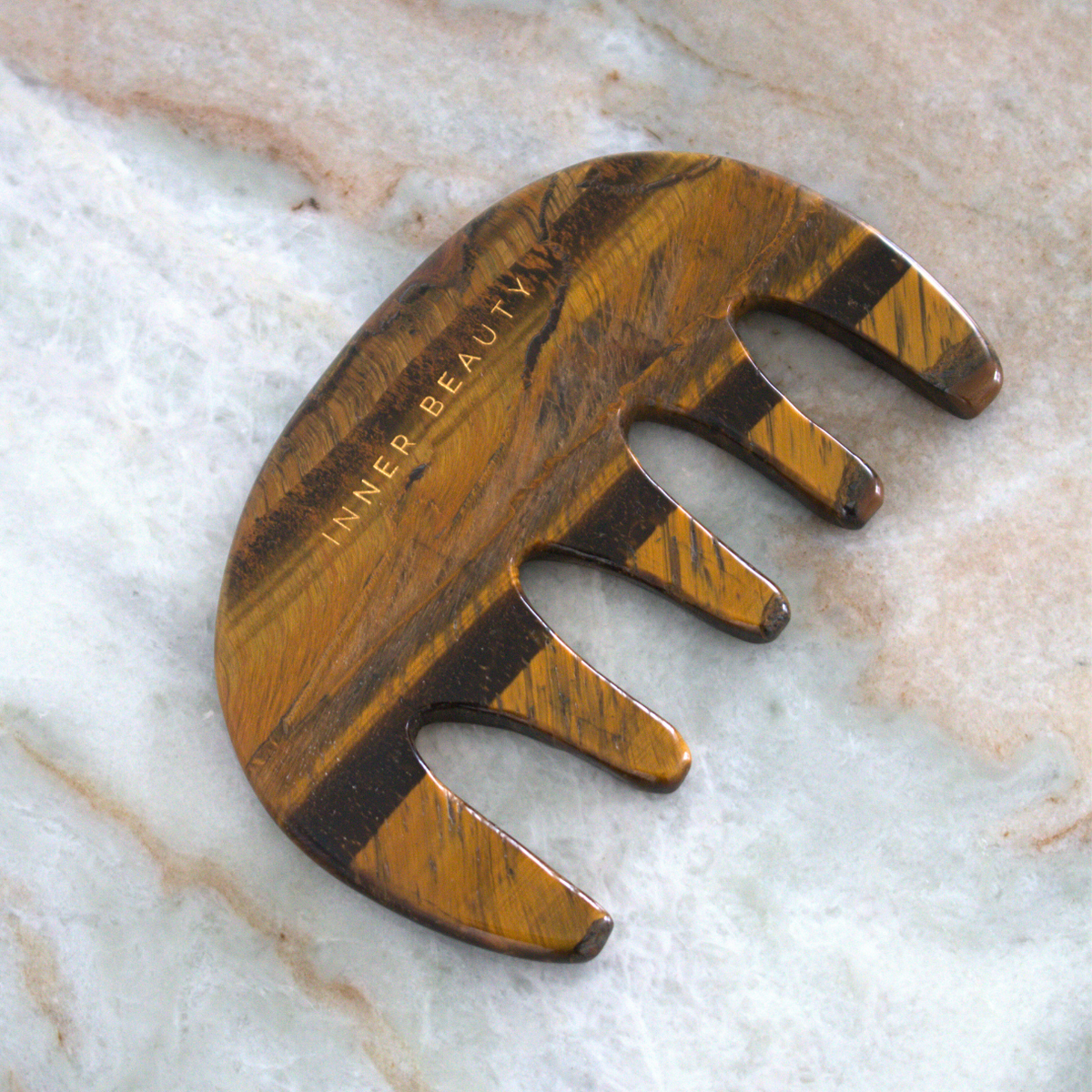 Hand-carved tiger's eye gua sha comb on marble, showing natural stone banding
