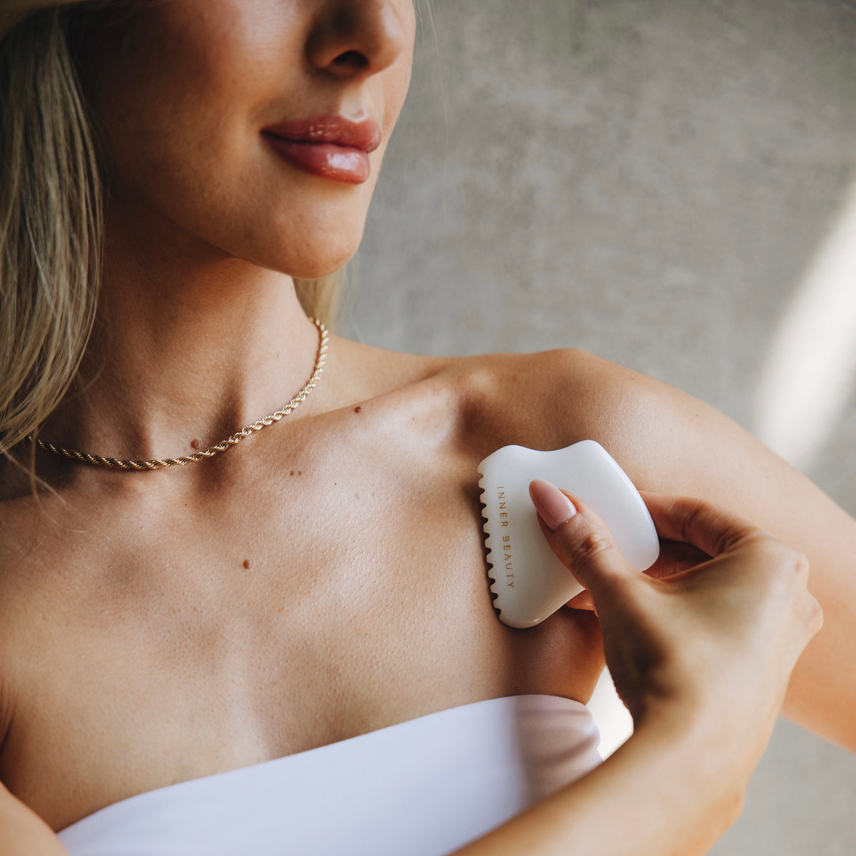 Woman using the four-edge white jade gua sha on her upper chest