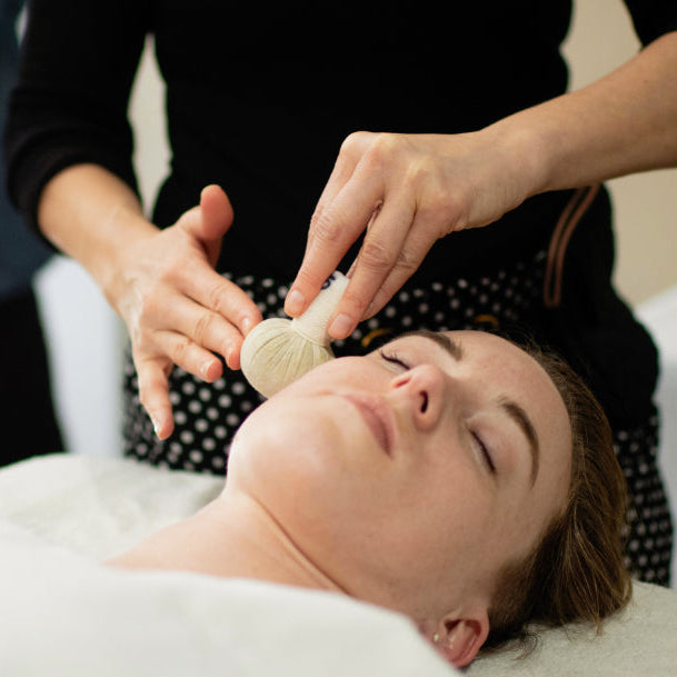 Esthetician using a Thai herbal poultice on a client's face