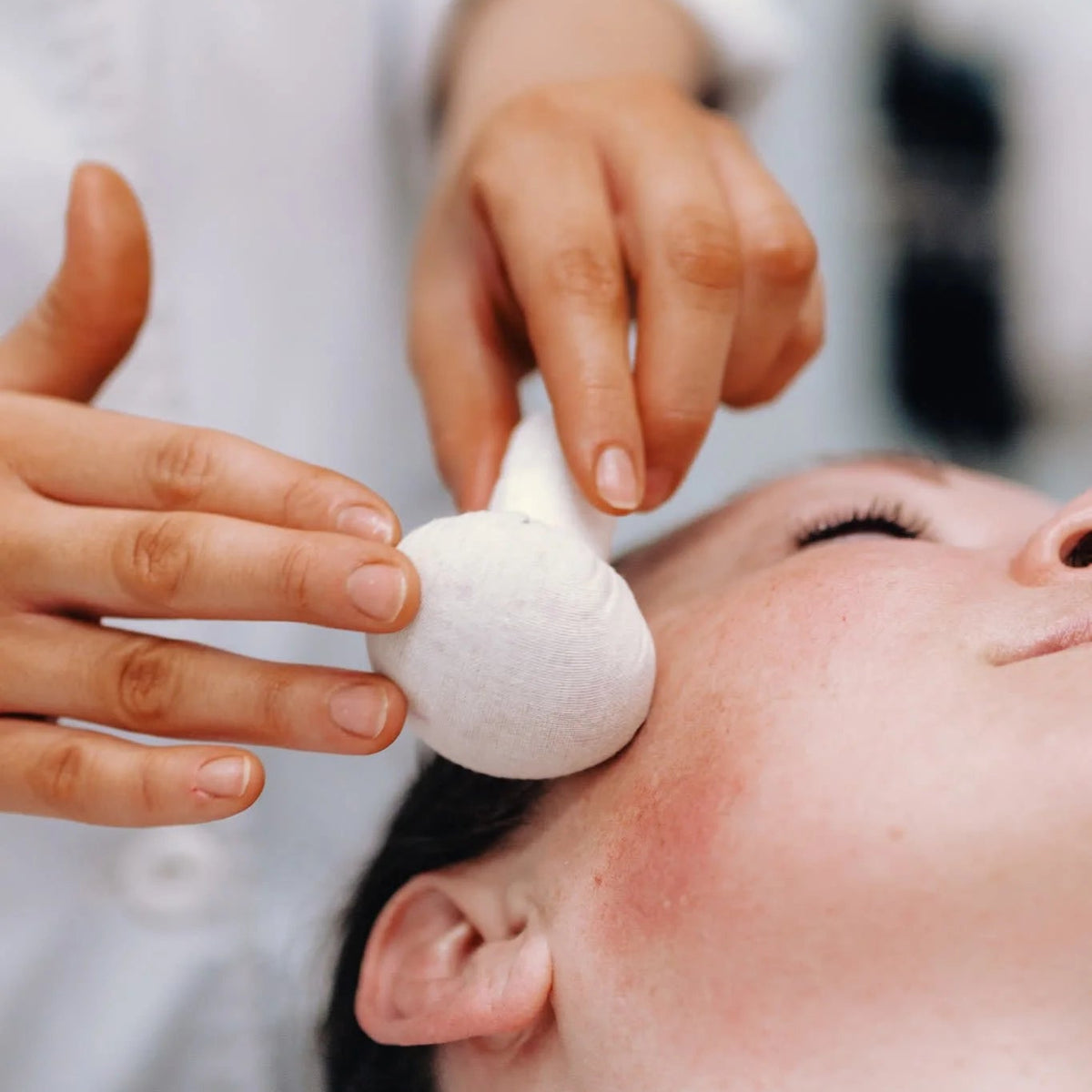 Warm herbal poultice pressed on the cheek during a facial