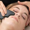 Esthetician using the CJB Pro Nephrite gua sha on a client's face
